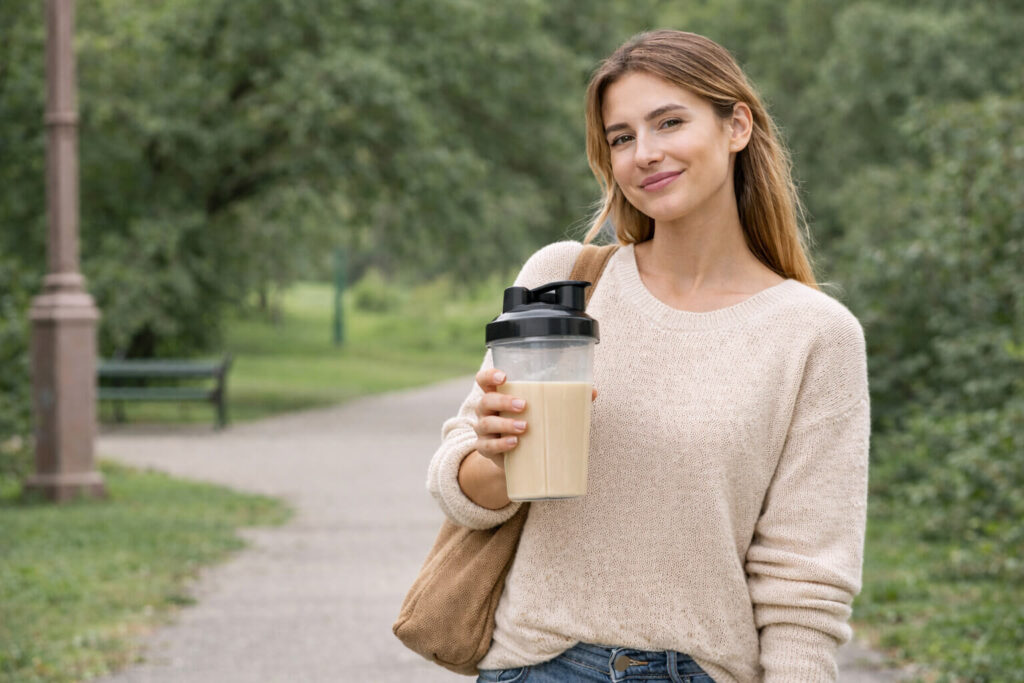 Mulher jovem segurando uma shakeira com whey protein em um parque